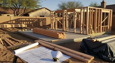 Framing on a concrete slab with lumber and building plans in the foreground