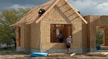 Workers building a wood-sheathed detached structure with a pitched roof