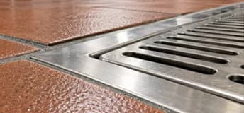 Stainless steel floor drain set into a red tiled commercial kitchen floor.