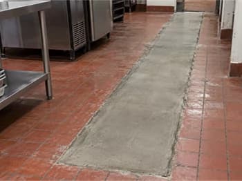 Concrete patch running through red tile flooring between commercial kitchen workstations.