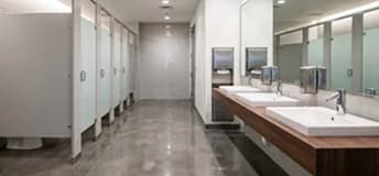 Commercial restroom with toilet partitions and a row of sinks beneath wall mirrors.