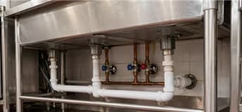 White drain piping and copper supply lines beneath a stainless steel sink.