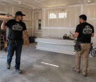 Two Big Horn Remodeling crew members preparing drywall in an unfinished garage.