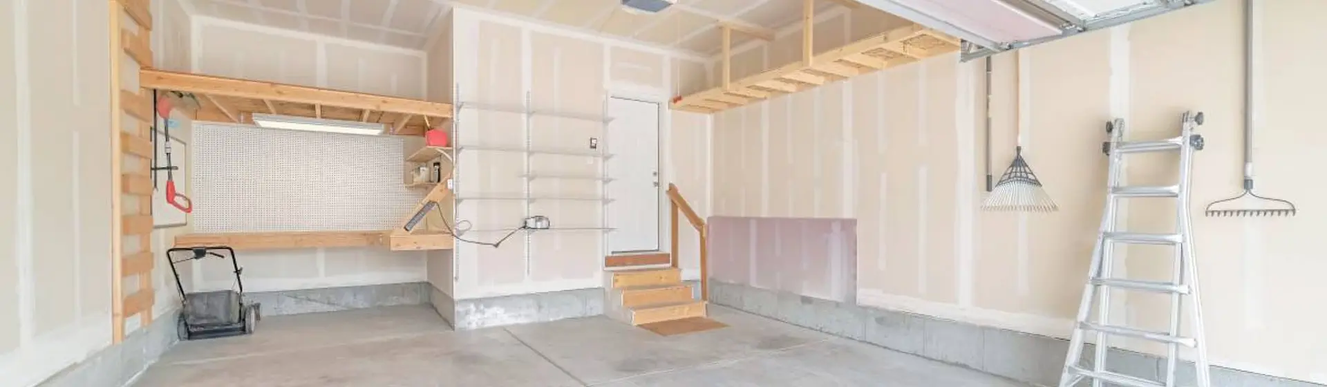 Unfinished garage interior with a workbench, storage loft, ladder, and open concrete floor.