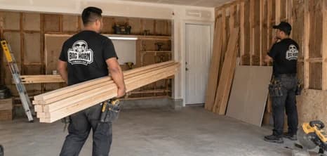 Big Horn Remodeling crew carrying lumber and preparing interior framing in an unfinished garage.