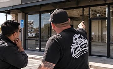 Two contractors reviewing a vacant commercial storefront from outside.