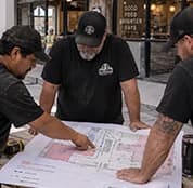 Three contractors reviewing a floor plan at a worktable.