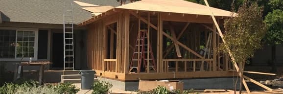 Framed home addition under construction beside an existing single-family home.