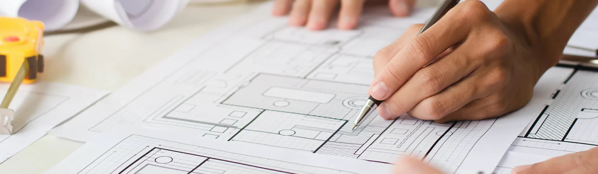 Hand marking a dimensioned floor plan with a pencil during drawing preparation.