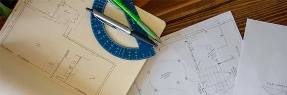Architectural floor plans with a blue protractor, pens, and drafting tools.