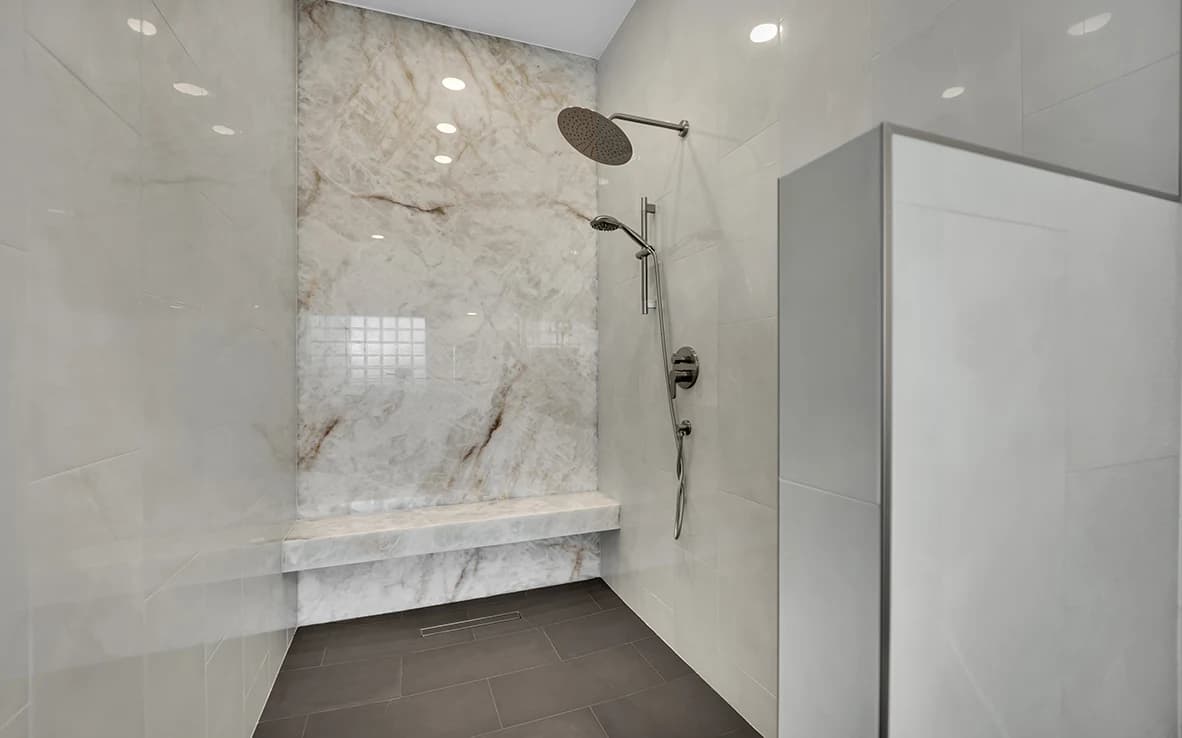 Onyx slab shower wall with bench, linear drain, rain head, and charcoal gray tile floor
