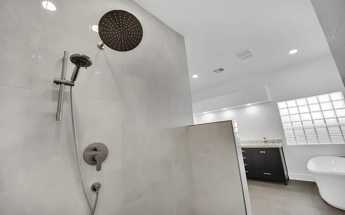 Rain head and handheld shower wand in a curbless primary shower with natural stone wall and charcoal floor tile