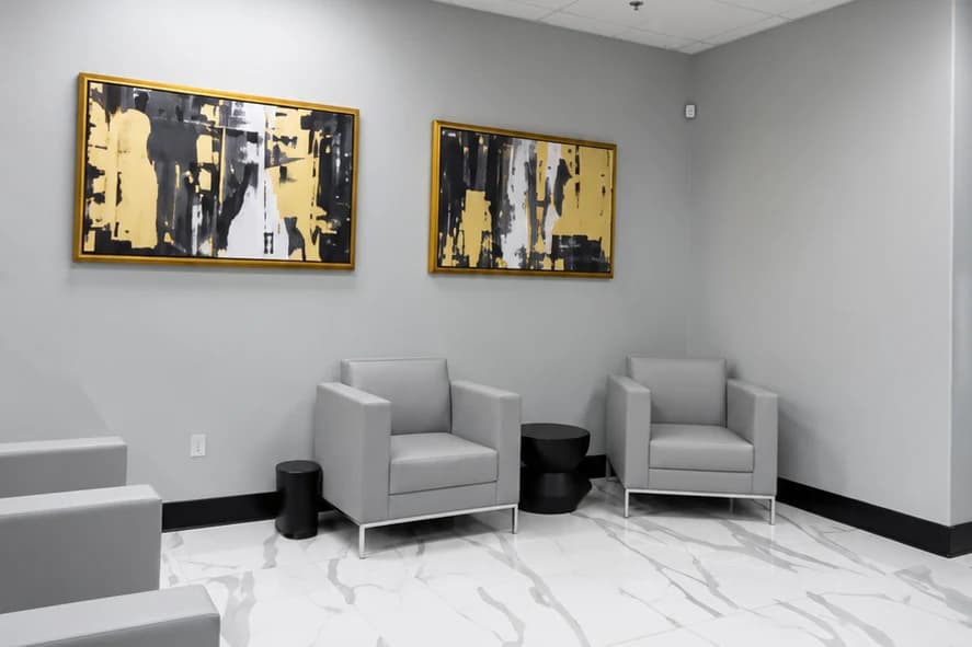 Ladah Law office reception with marble-look floor tile, gray armchairs, black side tables and framed artwork on gray walls.