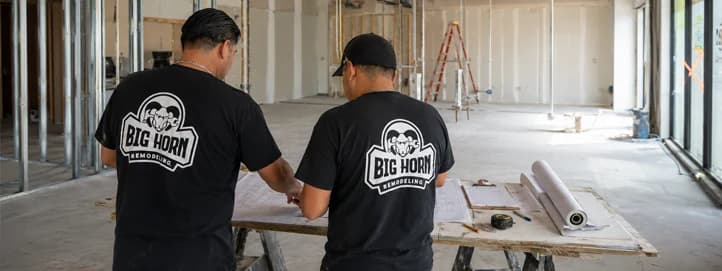 Two Big Horn Remodeling crew members reviewing plans at a worktable in an unfinished commercial tenant space