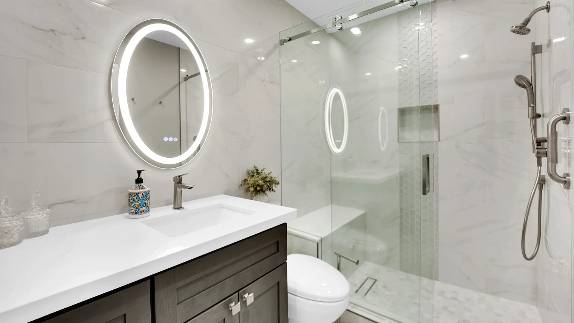 Finished bathroom remodel in Las Vegas with glass shower, vanity, round backlit mirror, and marble-look tile