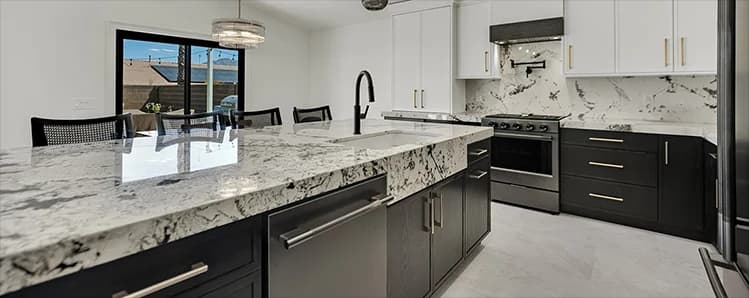 Finished kitchen with dark lower cabinets, white upper cabinets, stone countertops, slab backsplash, range, island, and black faucet