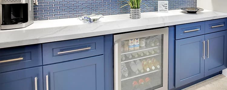 Blue base cabinets with beverage refrigerator, white countertop, and blue tile backsplash