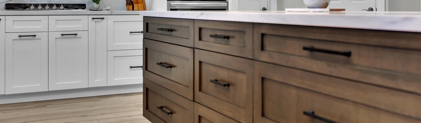 Close-up of a wood kitchen island with dark hardware, white perimeter cabinets, and light countertop