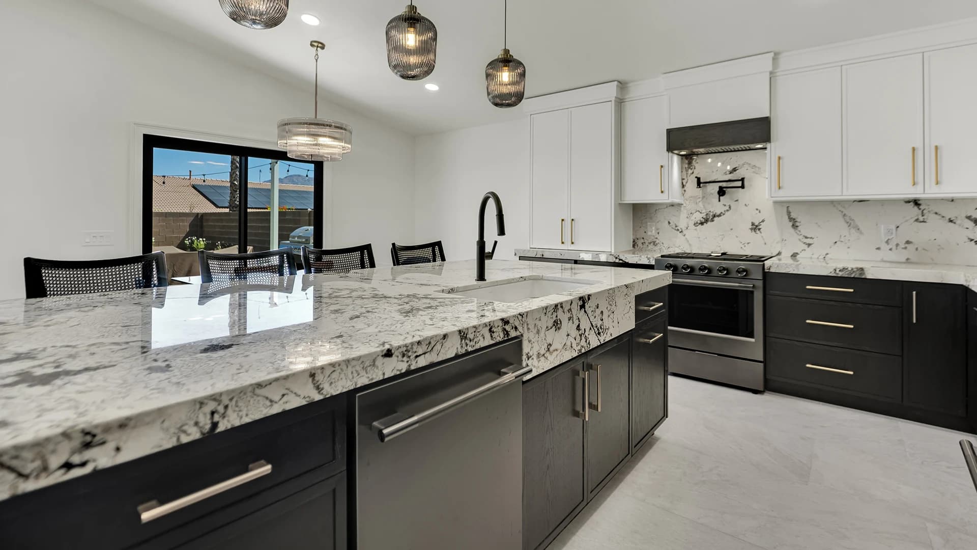 Luxury kitchen with dark island cabinets, white upper cabinets, black faucet, slab backsplash, range hood, and pendant lighting