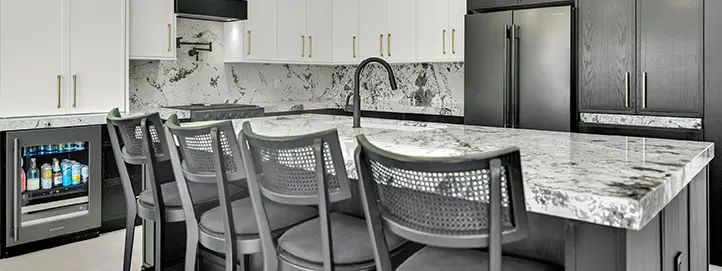 Large kitchen island with dark cabinets, stone countertop, black faucet, seating, and built-in beverage fridge