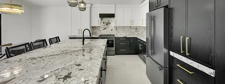 Luxury kitchen view with long stone island, black faucet, dark refrigerator wall, range wall, and pendant lighting