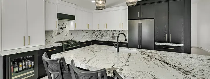 Wide view of a luxury kitchen with oversized island, white and dark cabinets, beverage fridge, range wall, refrigerator panels, and pendant lights