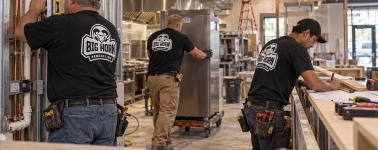 Three Big Horn Remodeling crew members coordinate plumbing, equipment and counter work inside a restaurant under construction.