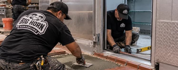 Big Horn Remodeling workers setting red floor tiles and checking the threshold at a walk-in cooler doorway.