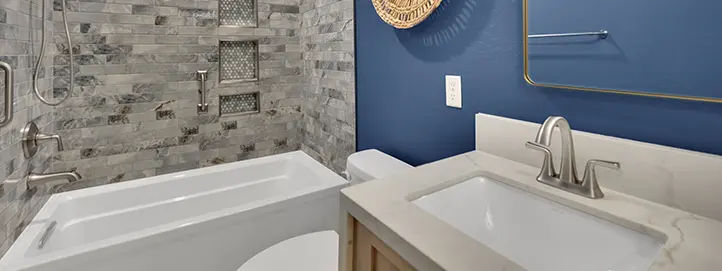 Bathroom with bathtub, gray shower tile, built-in niches, blue accent wall, and vanity