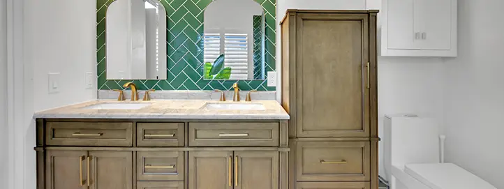 Bathroom with green herringbone tile, double vanity, tall storage cabinet, brass fixtures, and toilet