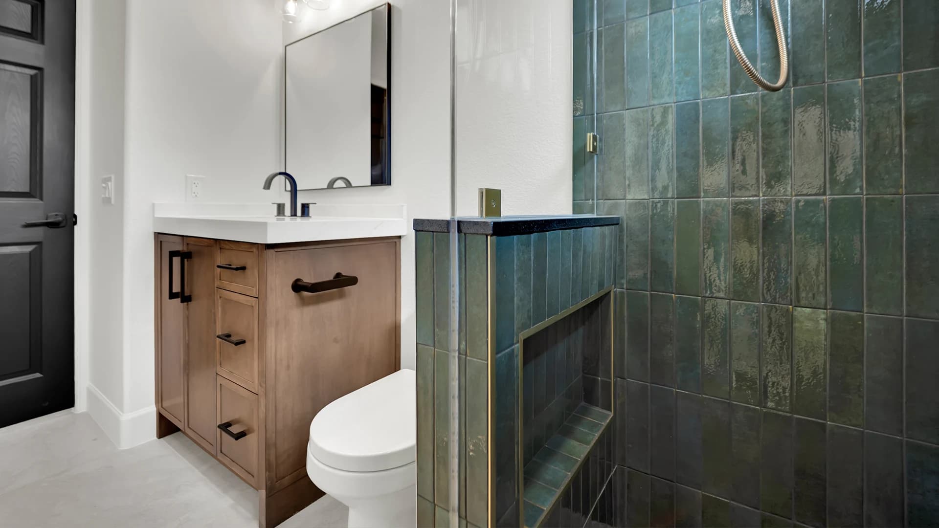 Bathroom remodel with blue-green tiled shower, wood vanity, black fixtures, and toilet