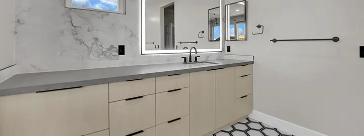 Bathroom with long vanity, backlit mirror, black grab bar, and patterned floor tile
