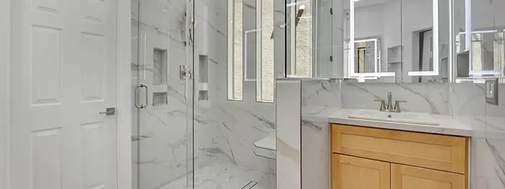 Bathroom remodel with marble-look glass shower, wood vanity, and lighted mirrors