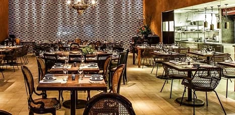 Finished restaurant dining room with set tables and an open commercial kitchen