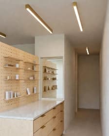 Light wood retail counter with wall-mounted display shelves and linear ceiling lights.