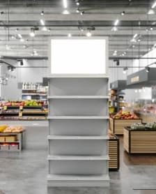 Freestanding gray display shelves in a grocery store beneath ceiling track lights.