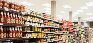 Stocked grocery-store aisles beneath bright rectangular ceiling lights.