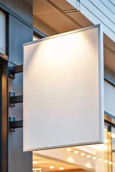 Blank projecting storefront sign attached to metal wall brackets.