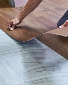 Hands positioning flexible wood-look flooring over the subfloor.