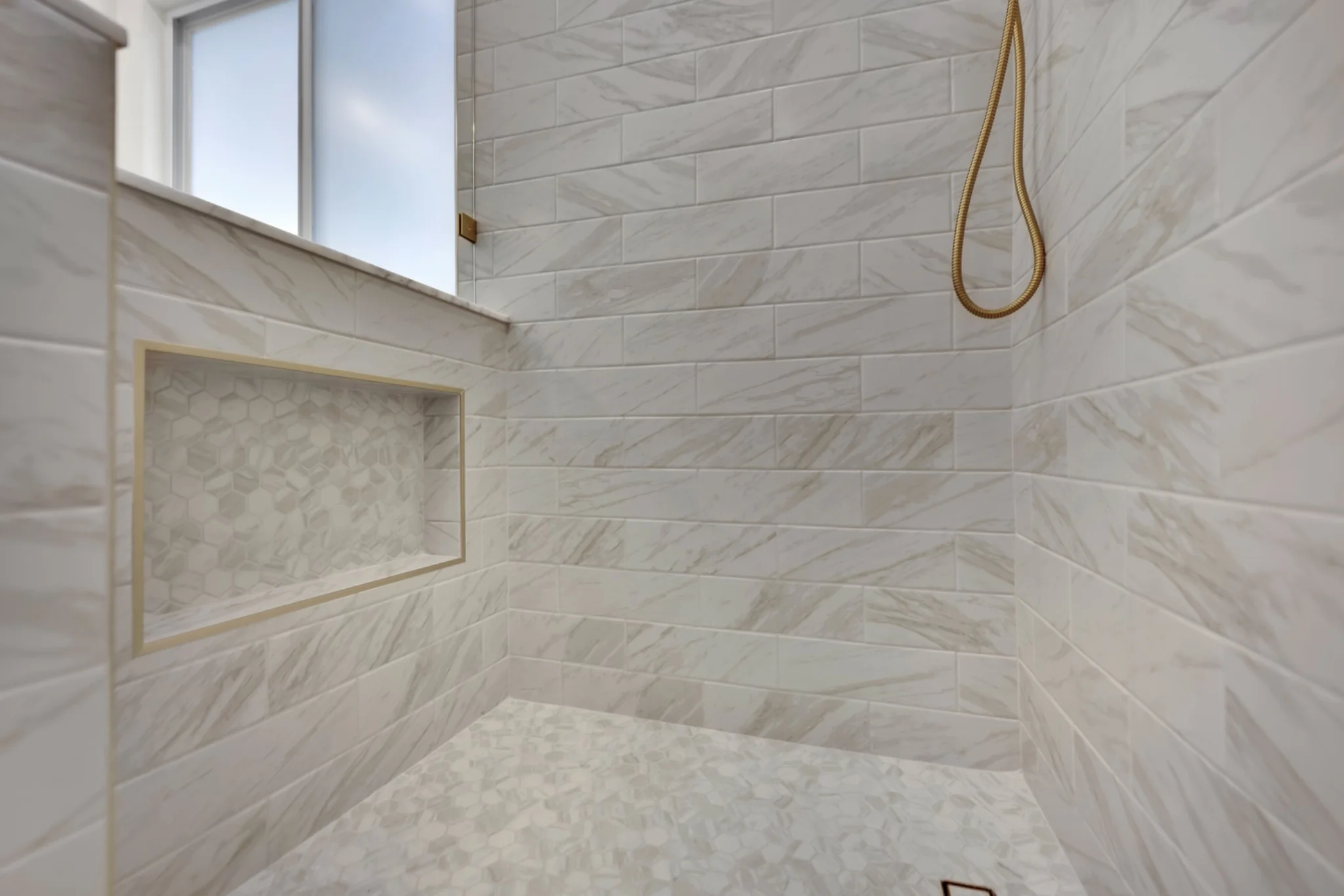 Marble shower niche with brass trim and matching mosaic tile