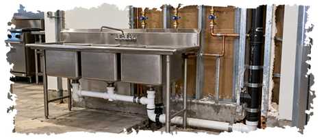 Exposed copper water lines and white drain piping behind a stainless steel three-compartment sink.