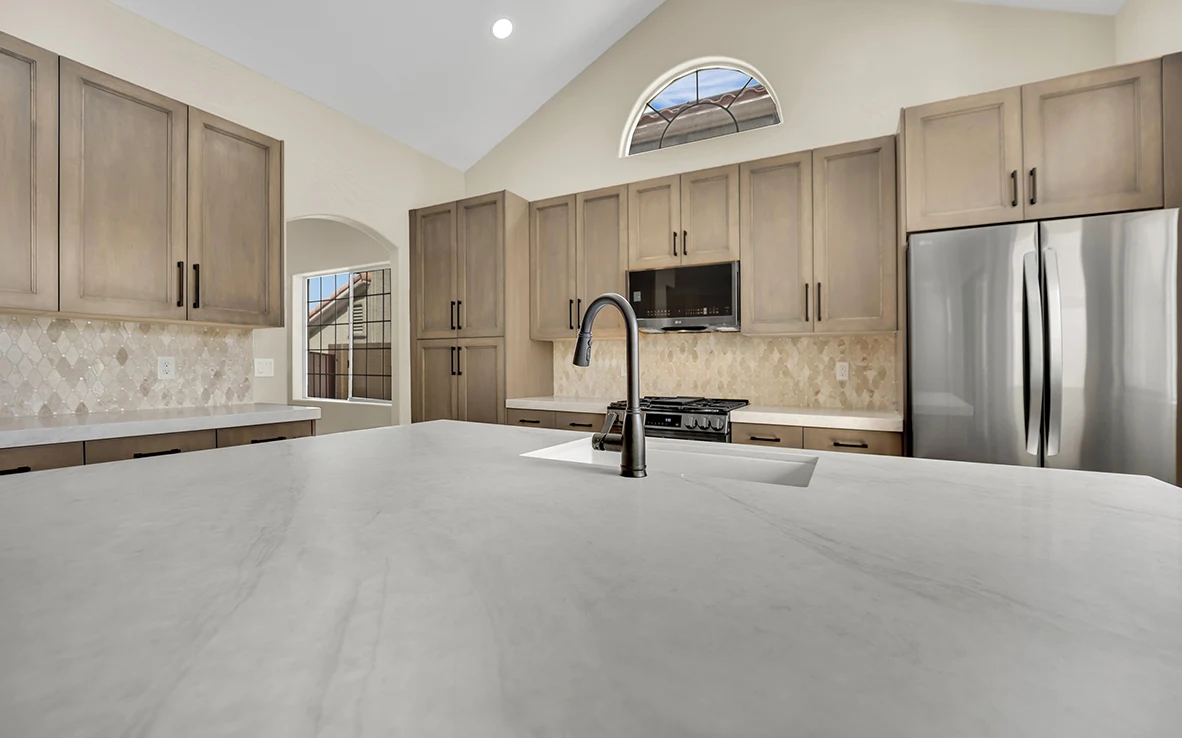 Wide Briella Gold quartz island with black faucet and sample-matched maple cabinets beyond