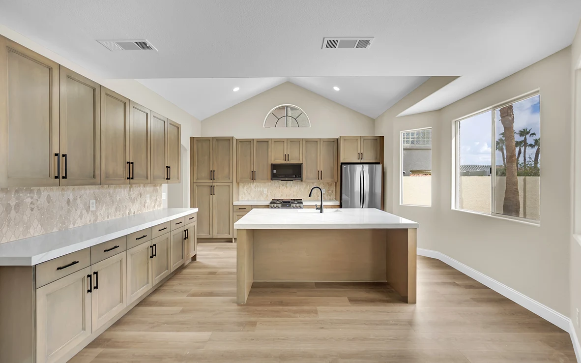 Wide view of Cantabria kitchen with freestanding quartz island, custom maple cabinets, and open floor area
