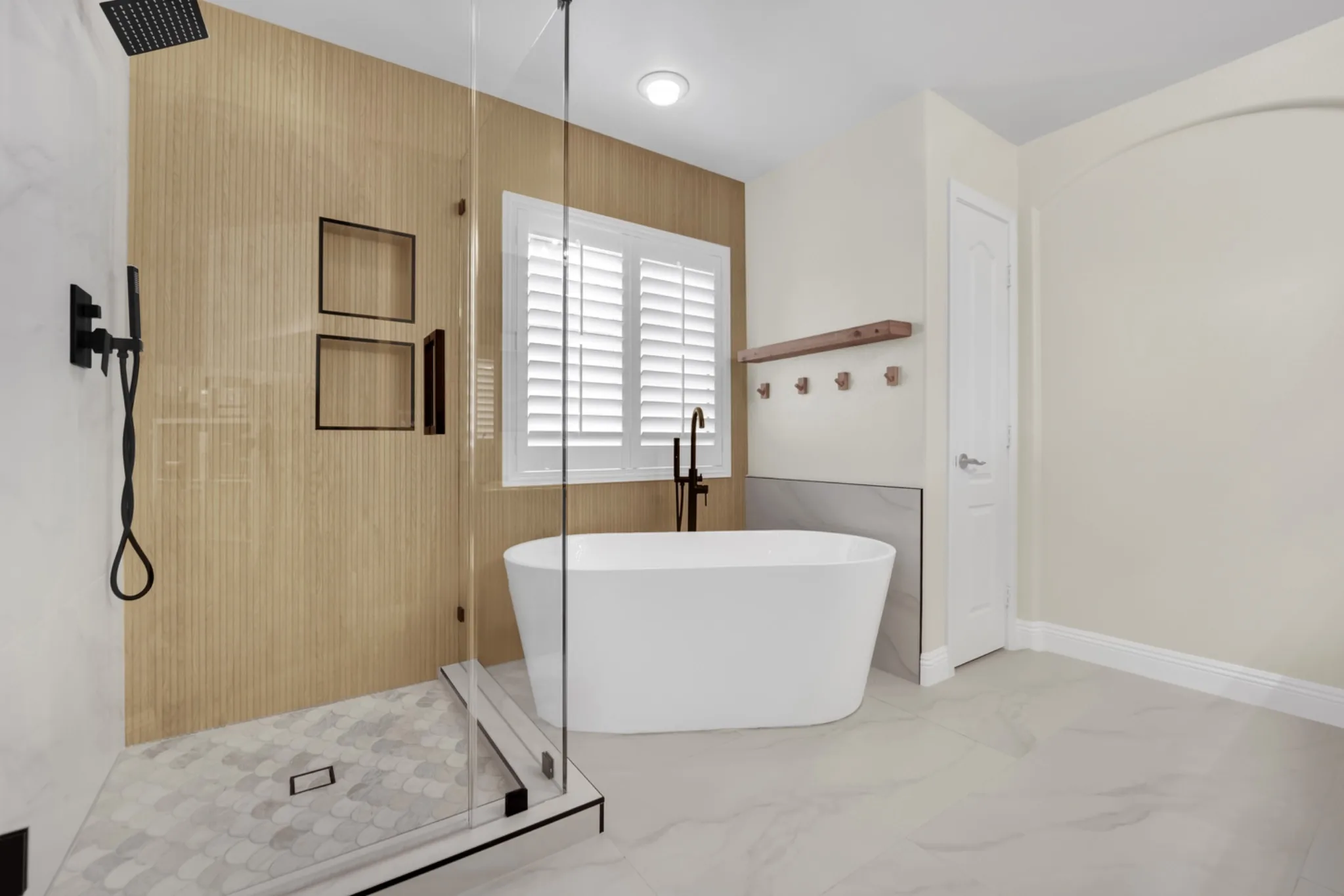 Primary bathroom remodel with freestanding Kohler tub, custom glass shower, wood-look wet wall tile, and matte black fixtures