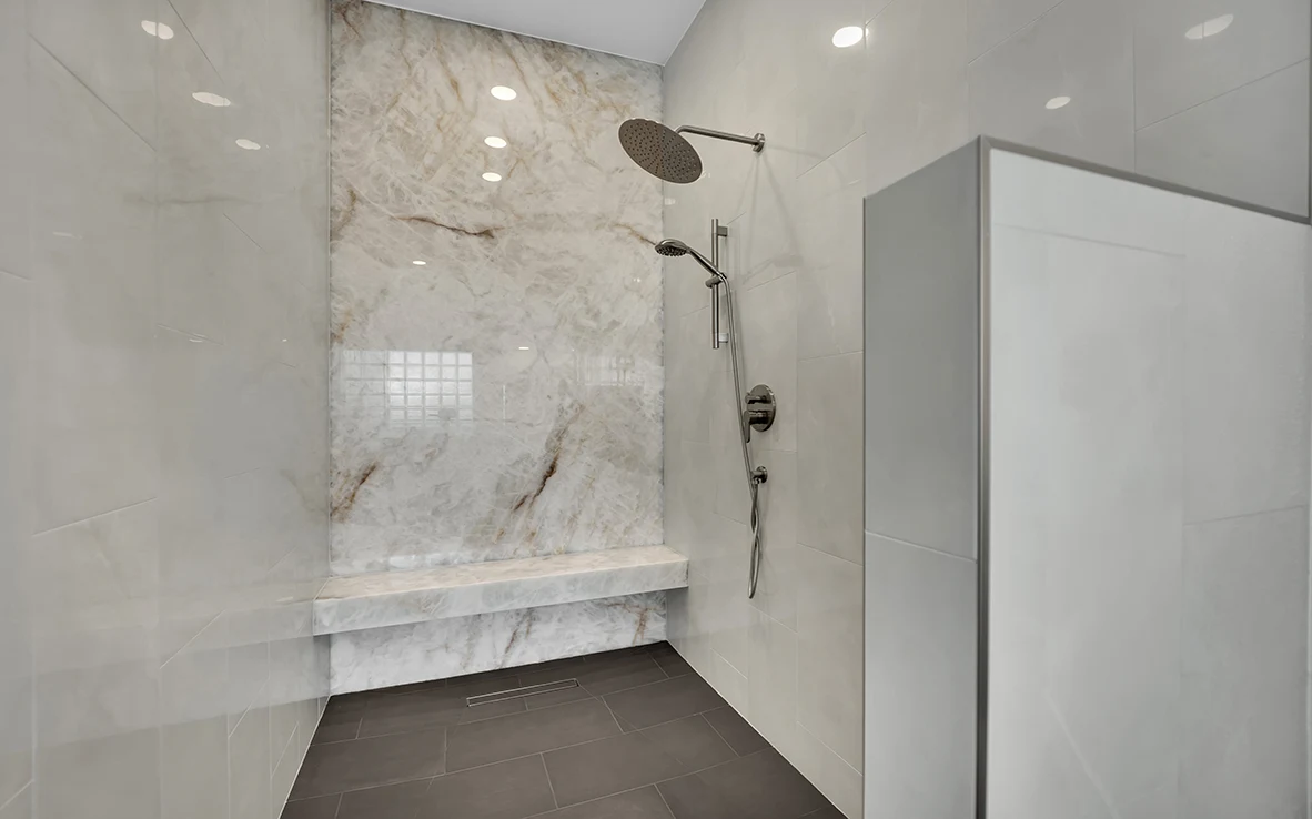 Onyx slab shower wall with bench, linear drain, rain head, and charcoal gray tile floor