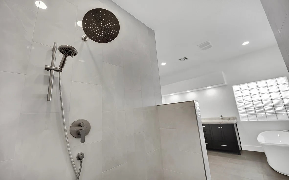 Rain head and handheld shower wand in a curbless primary shower with natural stone wall and charcoal floor tile