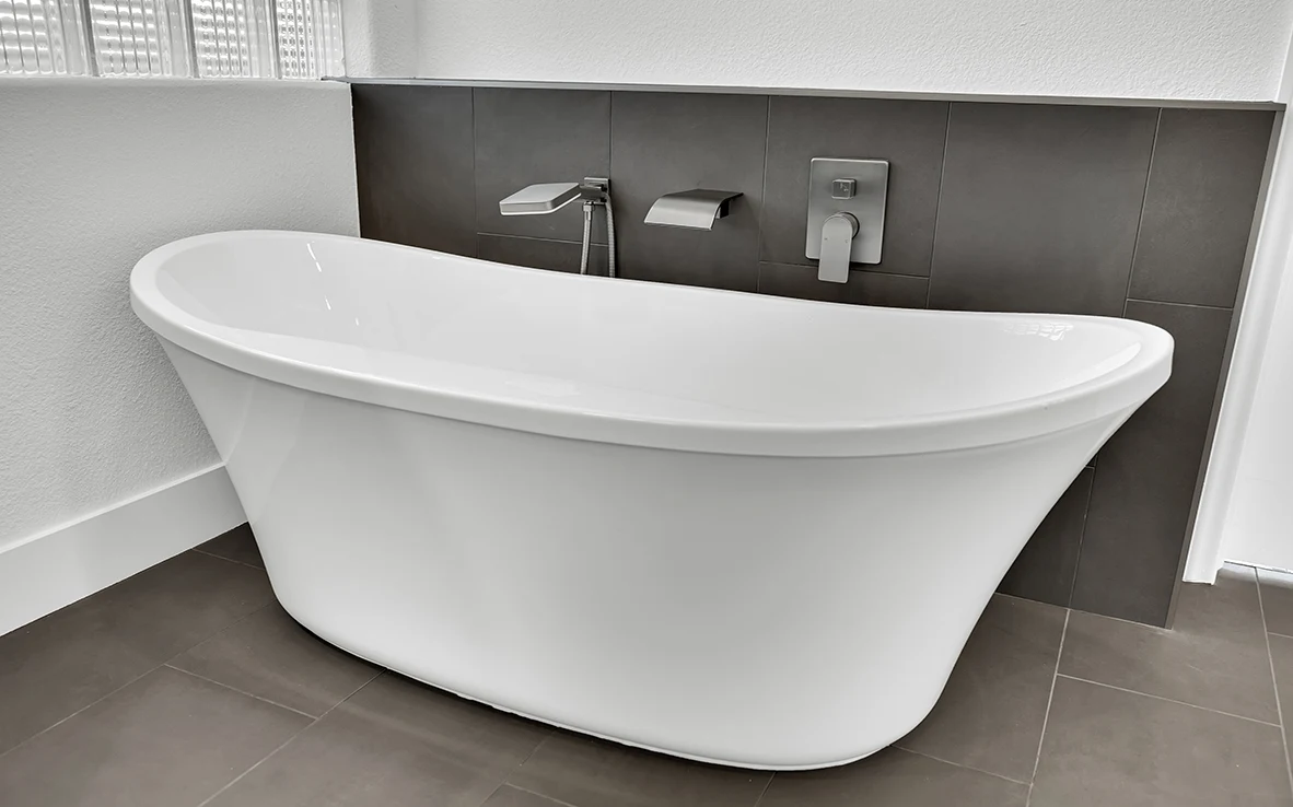 Relocated freestanding tub with charcoal gray tile floor, wall-mounted tub filler, and glass block window