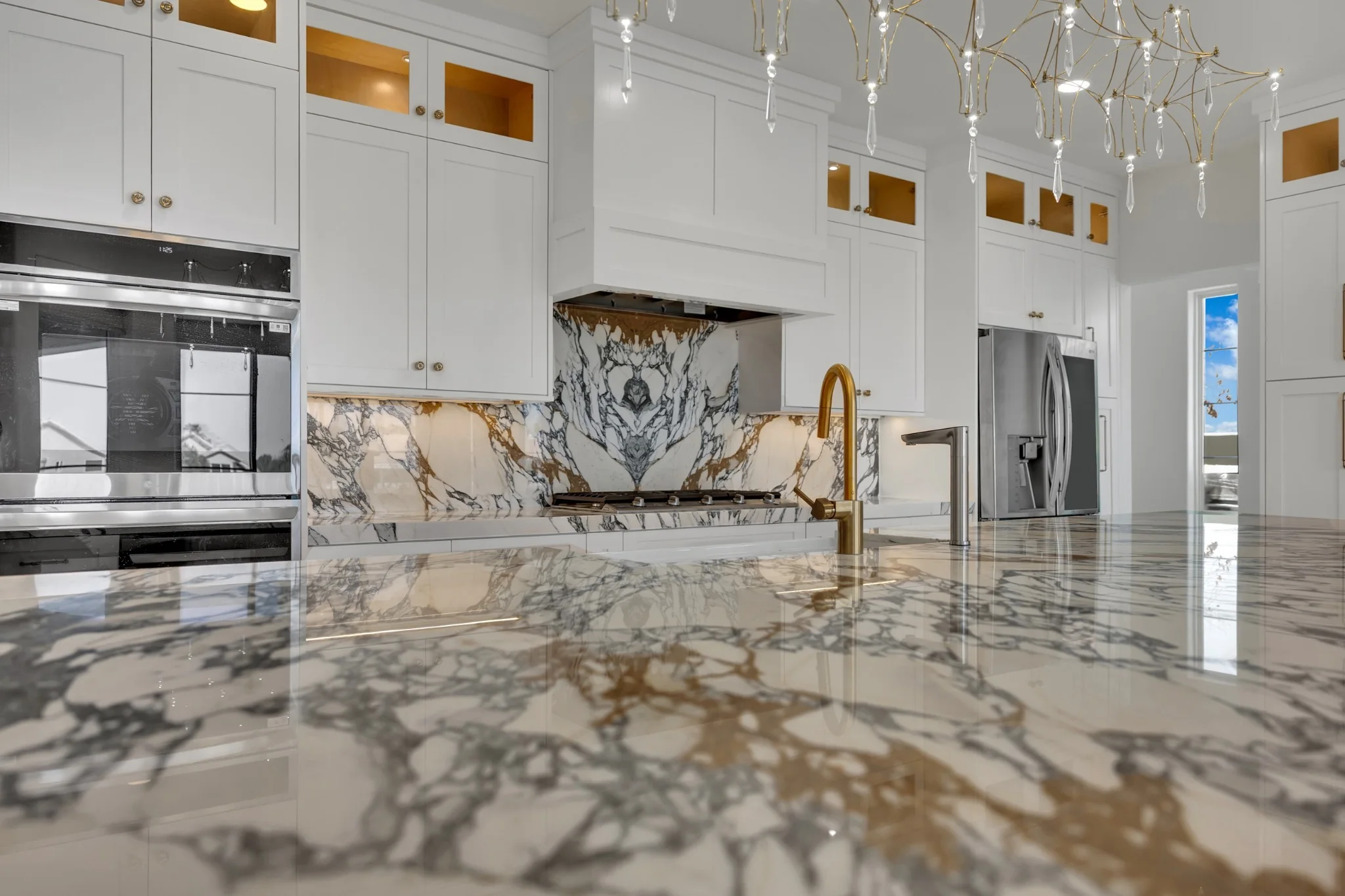 Custom white shaker cabinets with book-matched marble backsplash, gas cooktop, built-in ovens, and refrigerator wall in Desert Shores