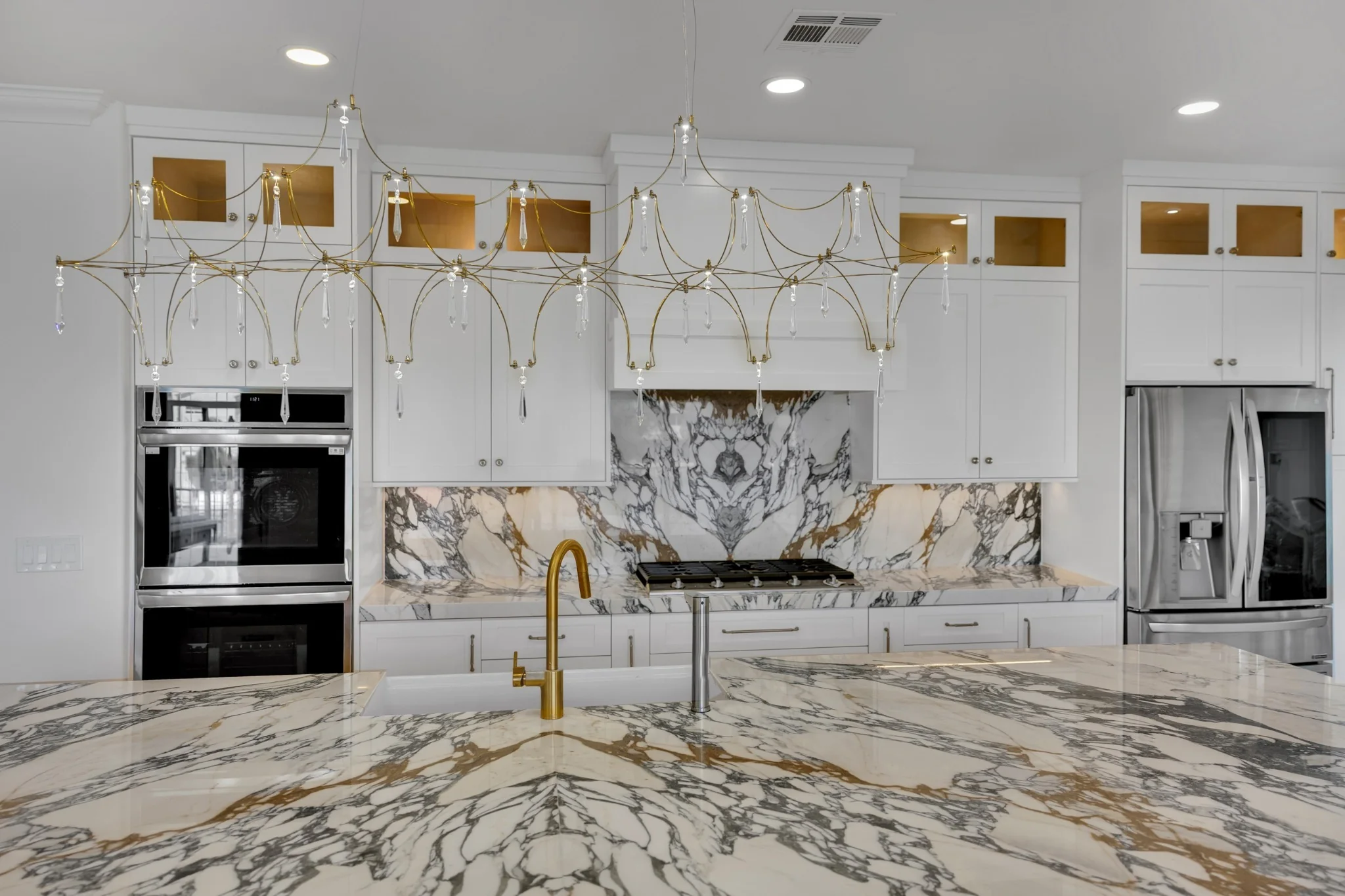 Luxury kitchen remodel with book-matched marble island, custom white cabinets, built-in ovens, and lakefront windows