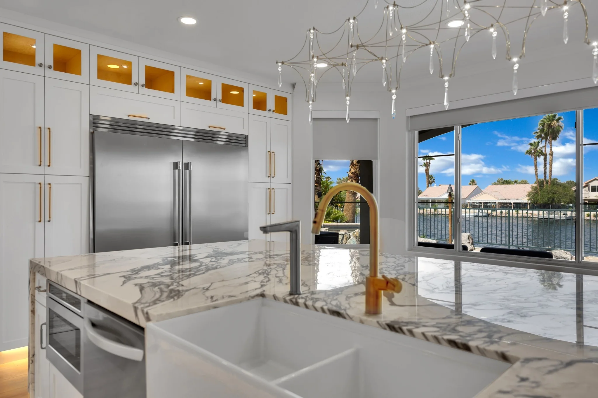 Waterfront kitchen remodel in Desert Shores with custom refrigerator wall, marble island, gold faucet, and lake view